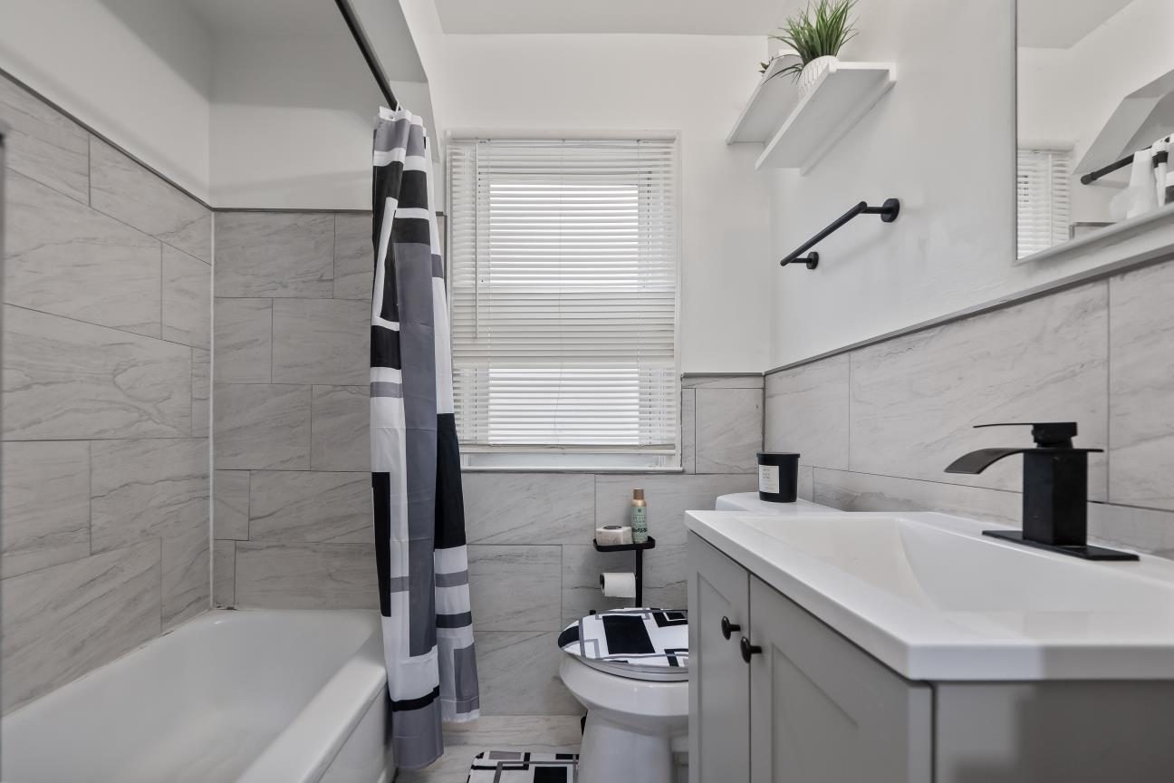 Renovated bathroom with large gray tile around the tub, tile wainscoting, a white vanity, and a black faucet