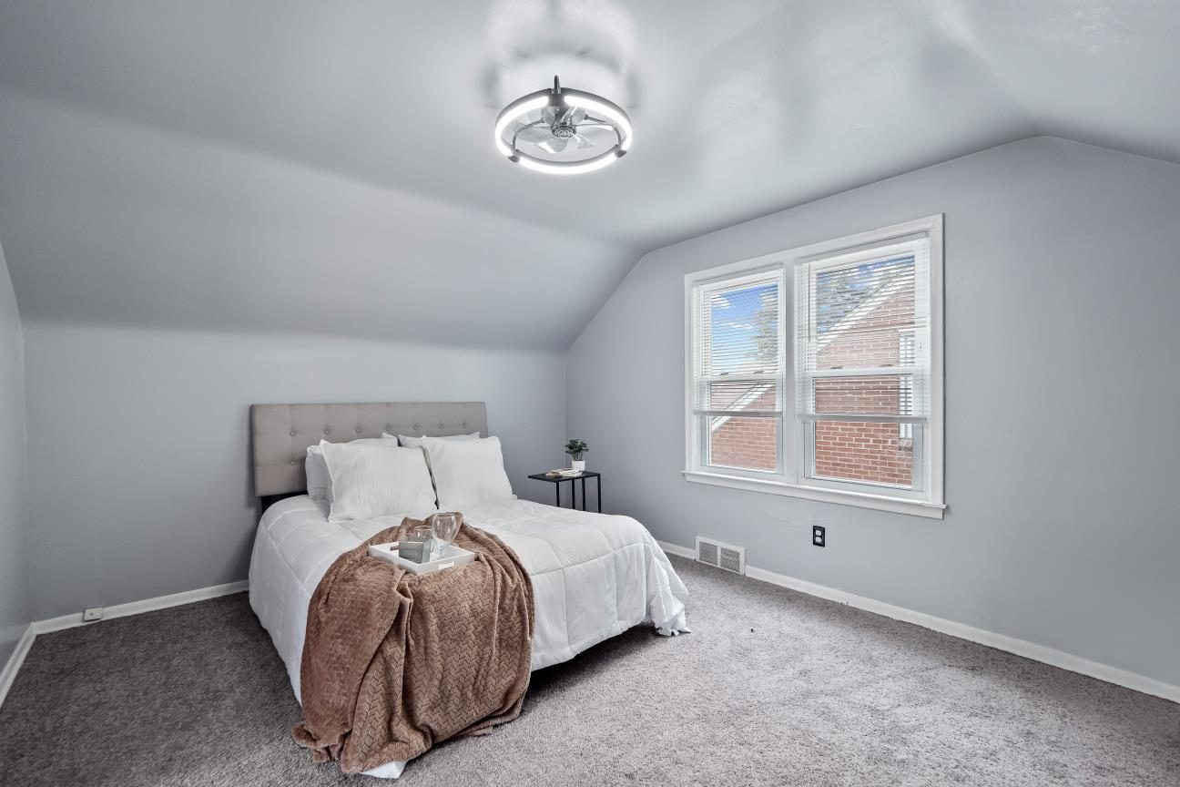 Upstairs bedroom under a sloped ceiling with new carpet, light gray walls, and a ceiling light