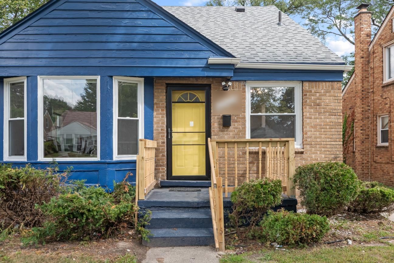 Close view of the front of the house: yellow front door, painted blue steps, new wood porch railings, white-trimmed windows, and blue siding above the brick