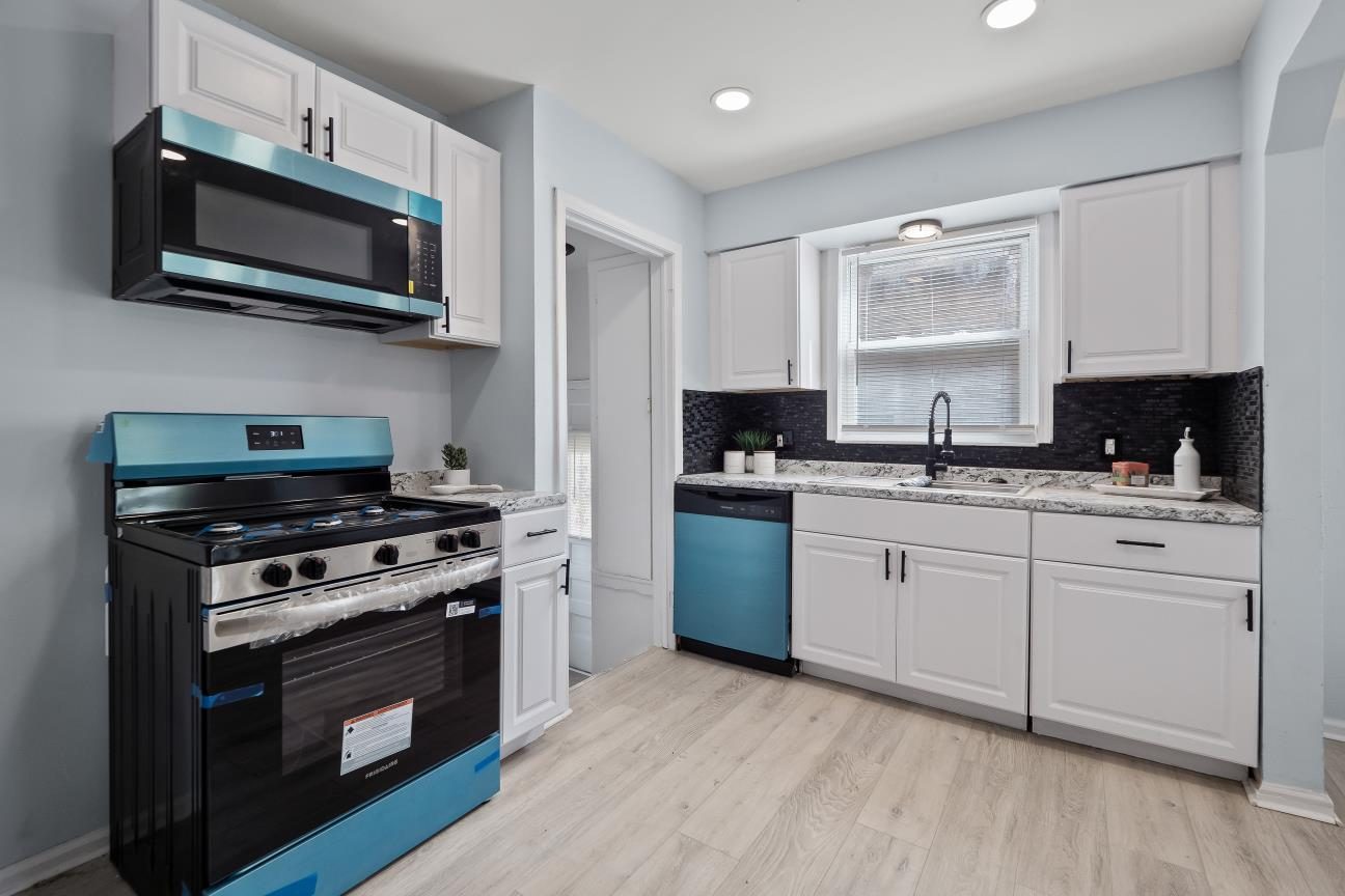 Second view of the kitchen with a stainless gas range, over-the-range microwave, dishwasher, white cabinets, and recessed lights