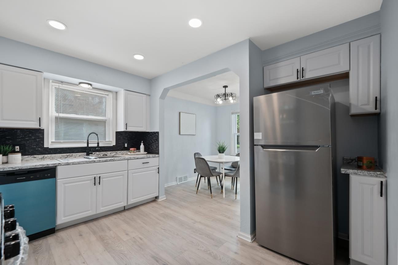 Renovated kitchen with white cabinets, black tile backsplash, granite-look counters, a black faucet, a stainless refrigerator, and an opening to the dining room