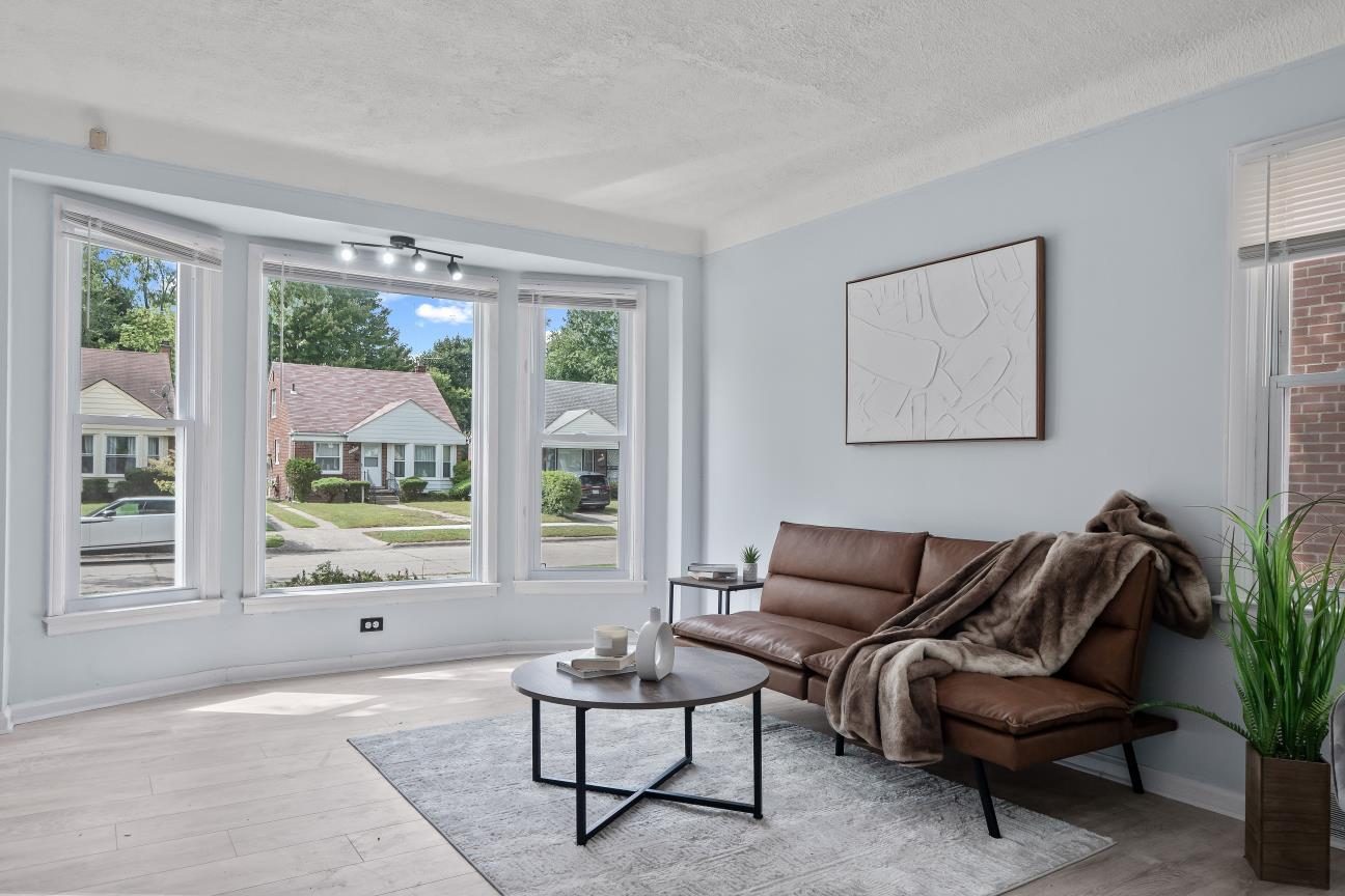 Living room with a three-window bay, light gray-blue walls, light wood-look plank floors, and a track light