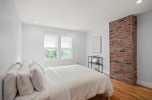 Bedroom with light hardwood floors, white walls, and an exposed red brick chimney column