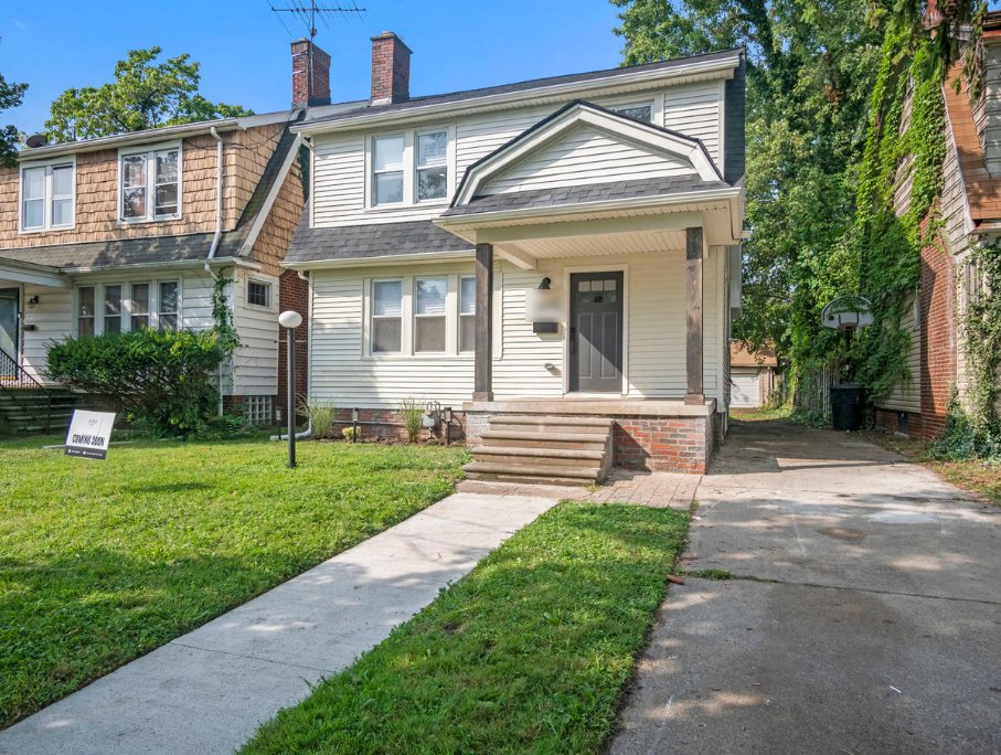 Renovated two-story house on Marborough in Detroit with cream siding, a gabled front porch with dark posts, a gray front door, brick steps, and a long driveway