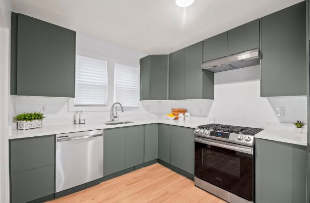 Renovated L-shaped kitchen with sage green flat-panel cabinets, white counters, a stainless range hood, gas range, and dishwasher, and light hardwood floors
