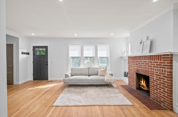 Living room with light hardwood floors, recessed lighting, white walls, and a red brick wood-burning fireplace