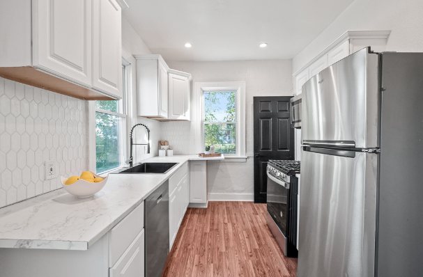 Second view of the kitchen showing a stainless refrigerator, white cabinets, hexagon tile backsplash, and a black interior door