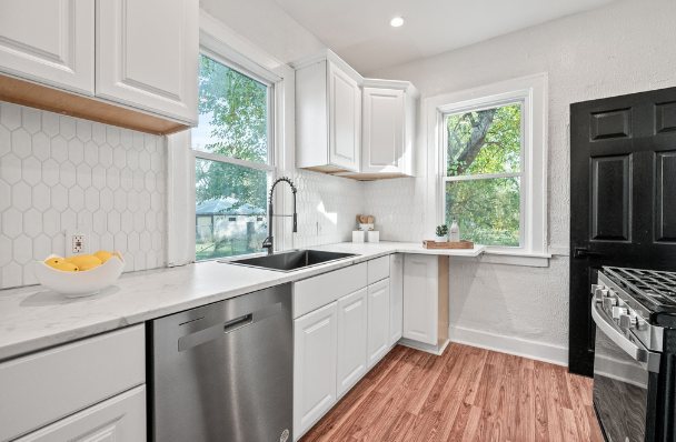 Renovated kitchen with white cabinets, hexagon tile backsplash, marble-look counters, a black faucet, stainless dishwasher and gas range, and wood-look floors