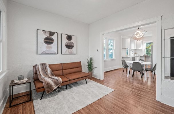 Living room with wood-look floors and white walls opening into a dining area with a pendant light