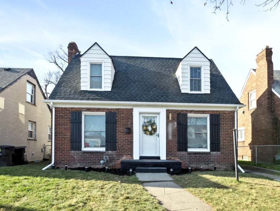 Renovated brick Cape Cod house on Stansbury in Detroit with white dormers, black shutters, a dark shingle roof, and a black front stoop