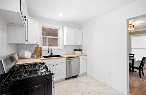 Renovated kitchen with white shaker cabinets, butcher-block counters, a black farmhouse faucet, stainless gas range and dishwasher, and marble-look tile floor