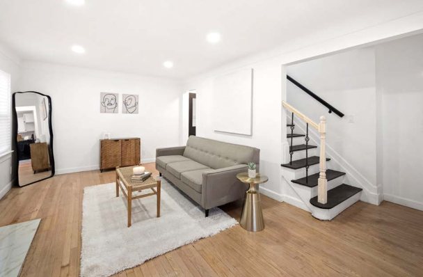 Living room with hardwood floors, recessed lighting, white walls, and a staircase with black-painted treads